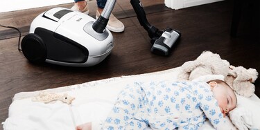 The VX8 vacuum works silently while a baby sleeps on a rug