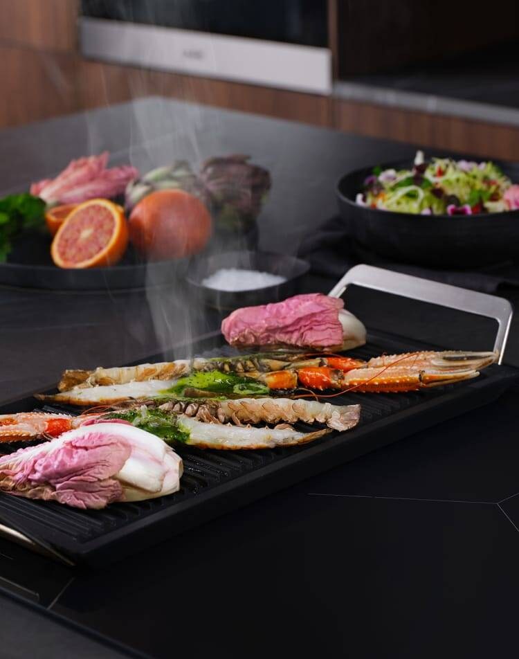 Different types of food is being prepared on an induction hob with the FlexBridge function.