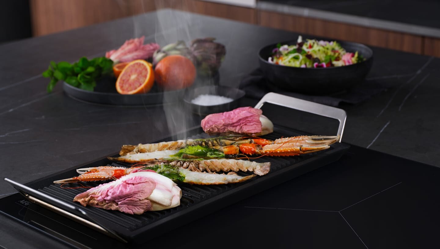 Different types of food is being prepared on an induction hob with the bridge function.