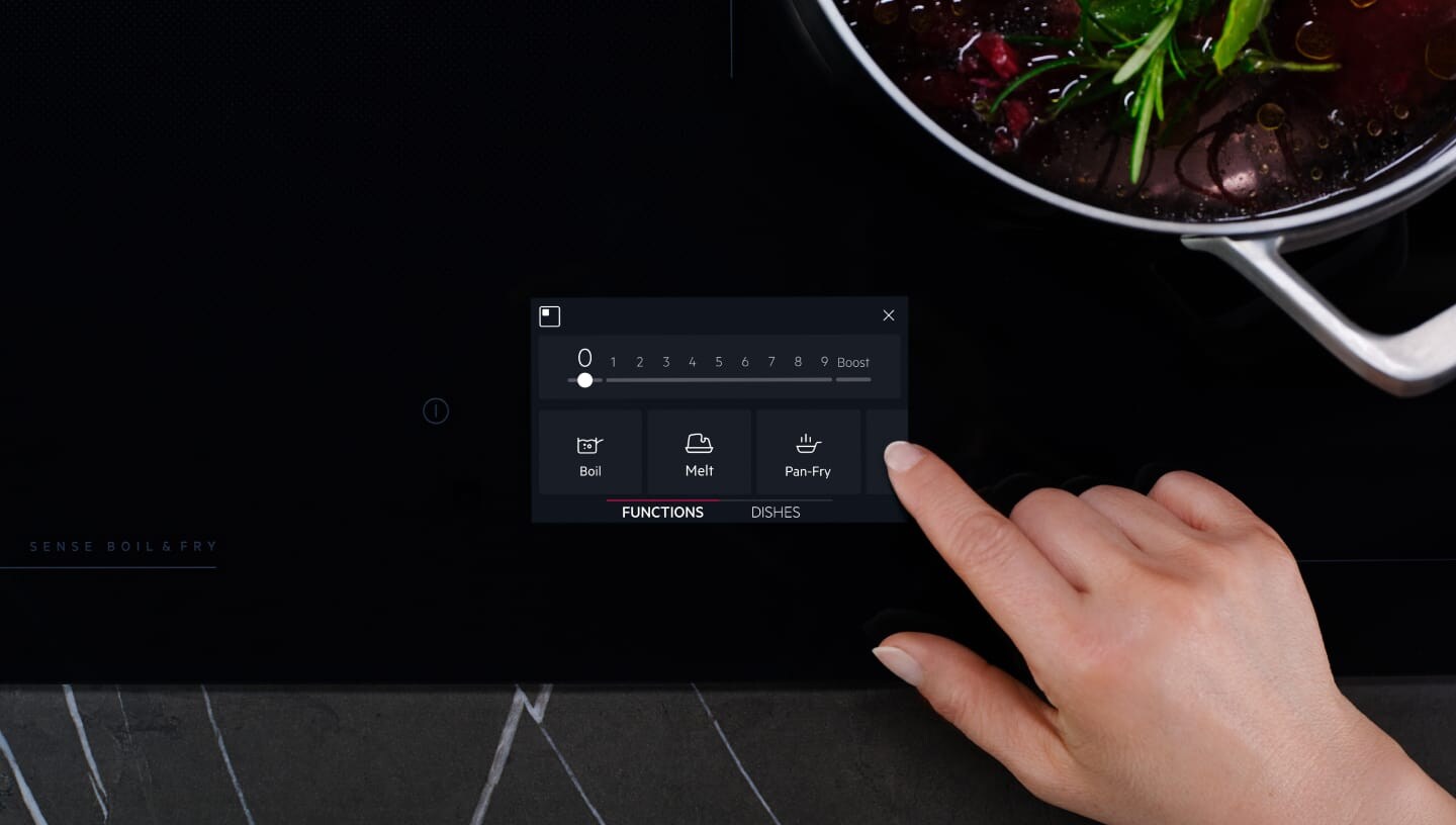 A finger is touching the control panel on an induction hob.