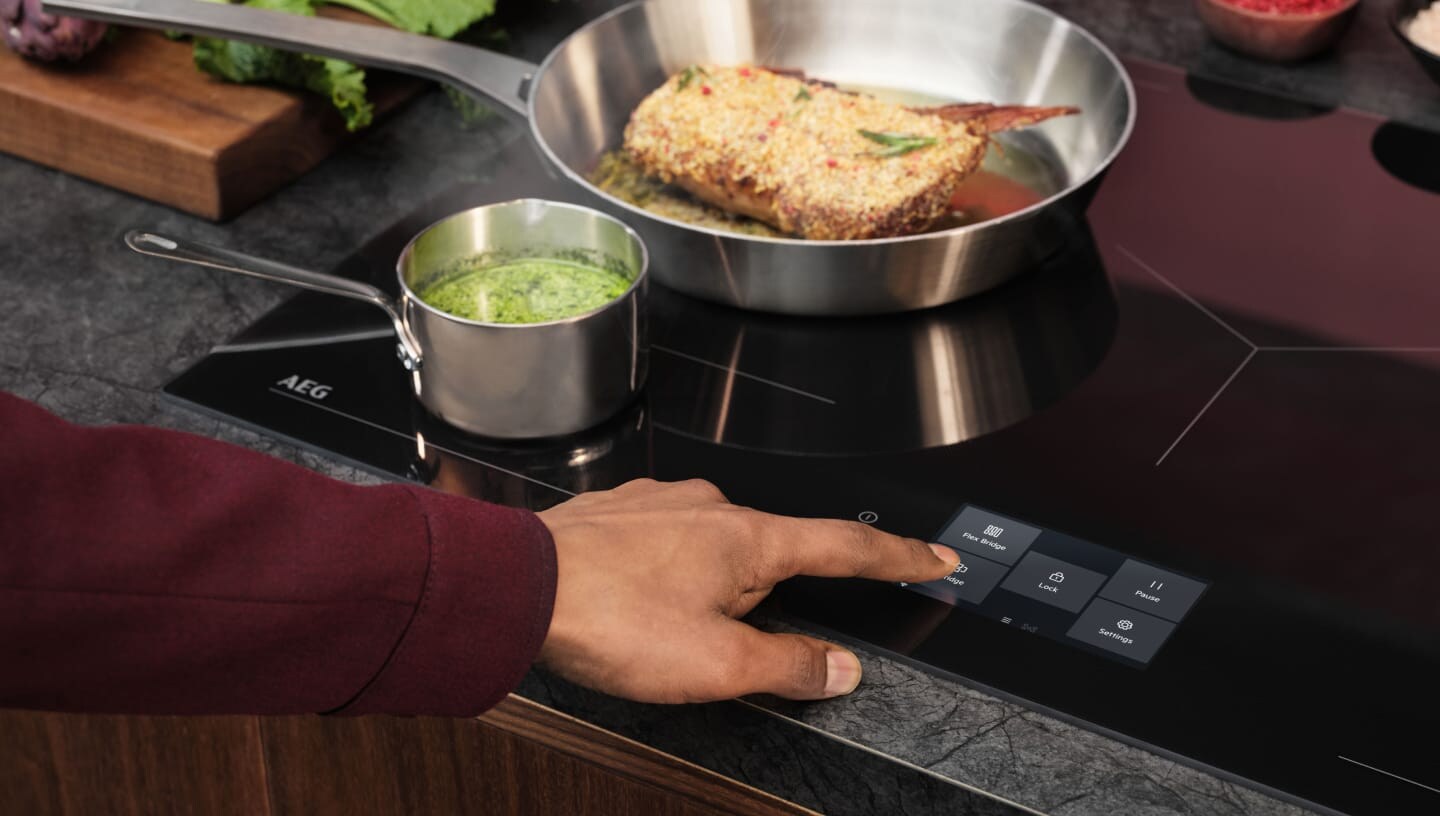 A finger is touching the control panel on an induction hob.