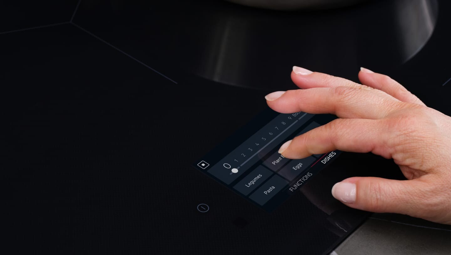 A finger is touching the control panel on an induction hob.