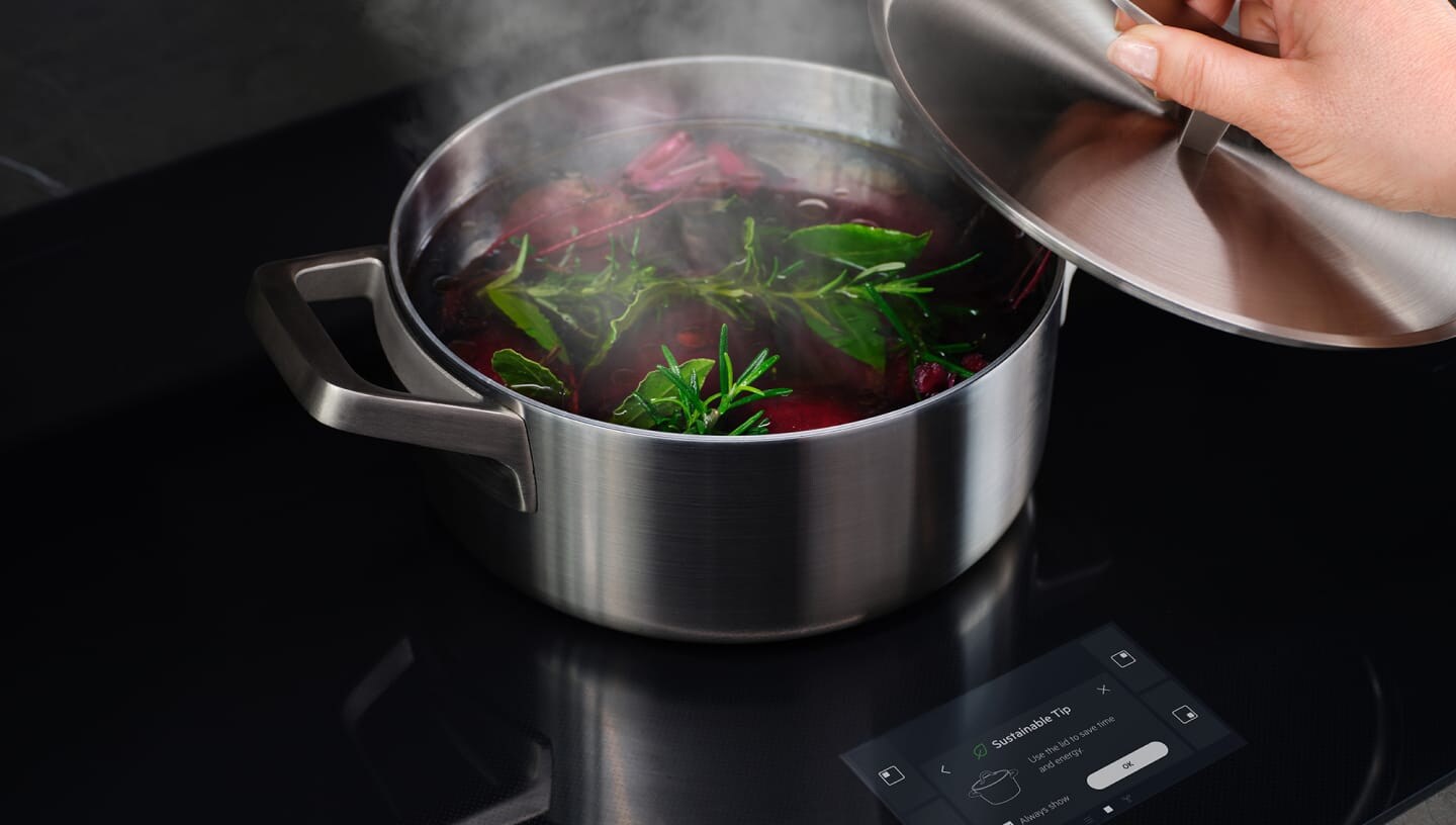 A hand is removing the pan lid of boiling vegetables.