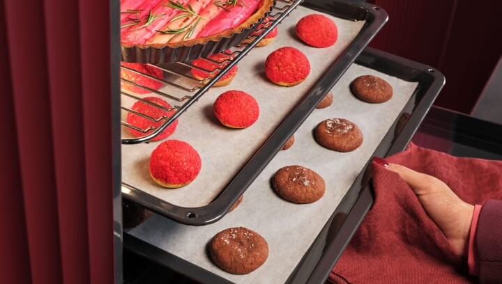 A person is taking a tray with pastries out of the oven.