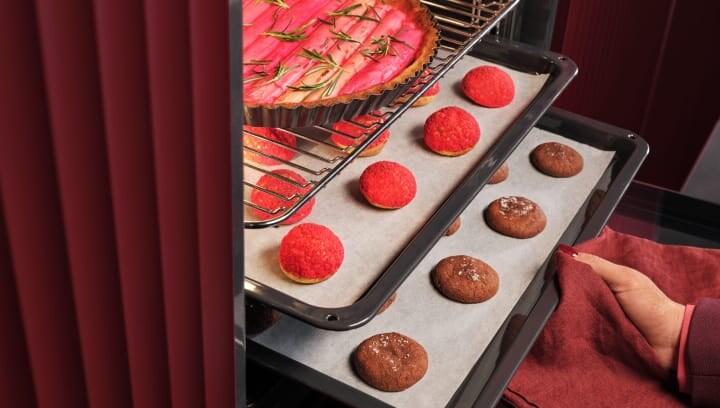 A person is taking a tray with pastries out of the oven.