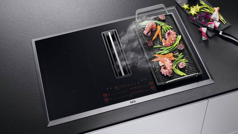 Food cooking on a plancha grill placed on an AEG hob.