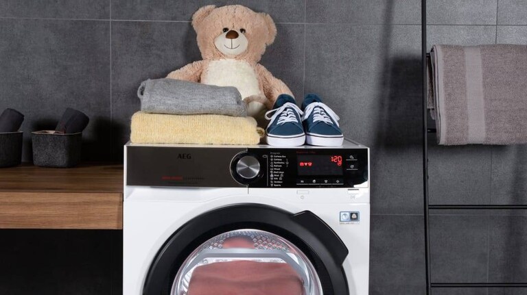 Teddy bear placed along with clothes and shoes on top of an AEG washing machine.